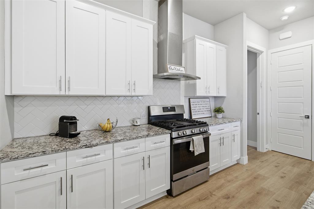 Kitchen featuring white shaker-style cabinetry, stone-finish countertops, herringbone-pattern tile backsplash, stainless steel range with matching vent hood, and wood-finish flooring