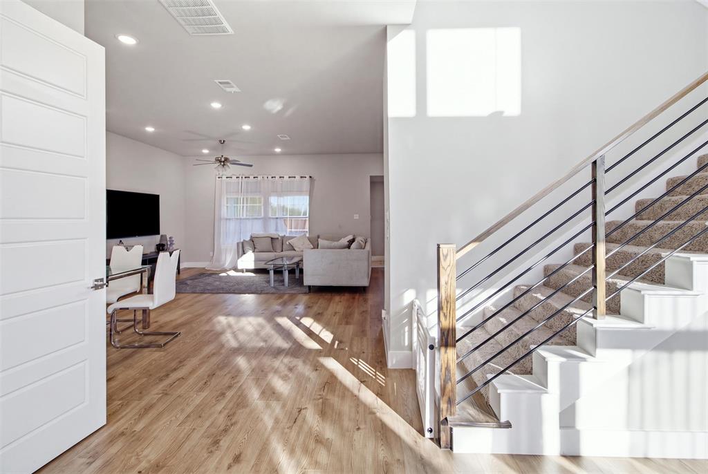 Open-concept interior featuring wood-finish flooring, recessed lighting, and a staircase with a wood handrail and horizontal metal balusters