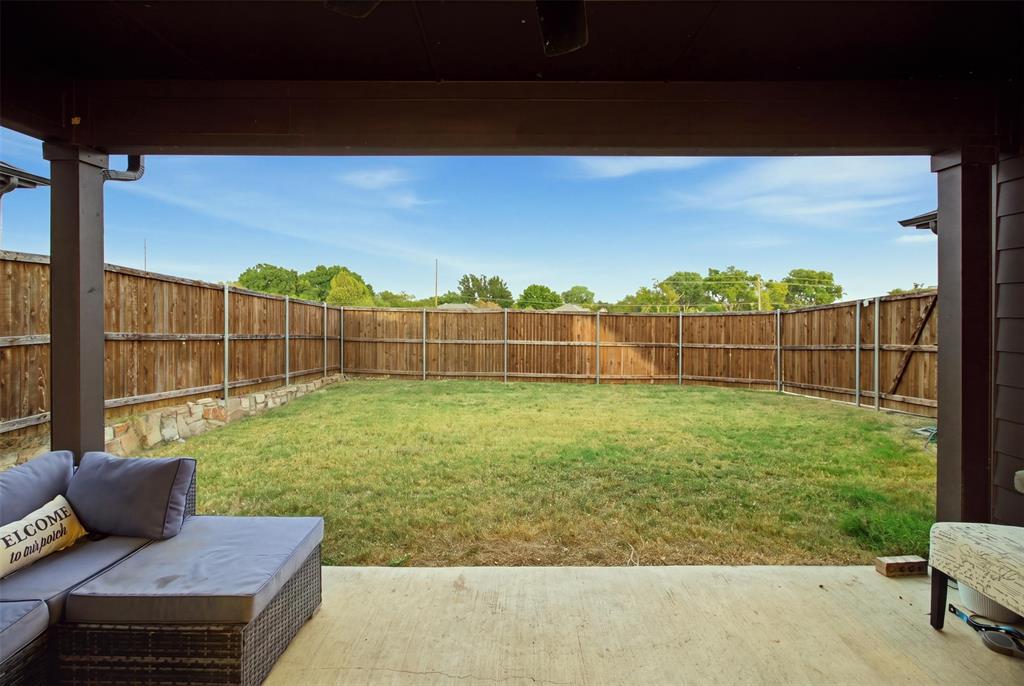 Covered patio featuring a concrete floor, stone-accented wood perimeter fencing, and an expansive lawn
