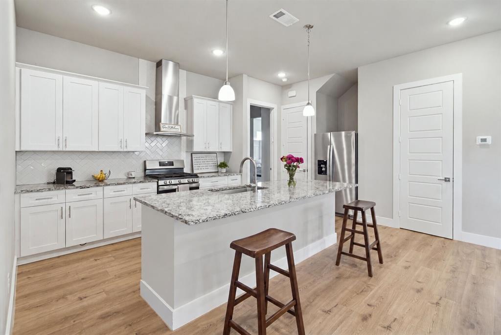 Kitchen featuring white cabinetry, stone-surface countertops, chevron-patterned backsplash, stainless steel appliances, and wood-finish flooring