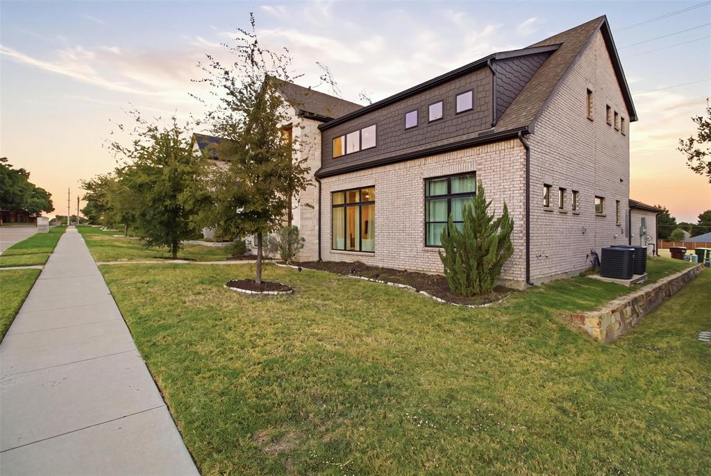 Two-story exterior featuring light-toned brick masonry, dark shingle siding, expansive picture windows, and a stone retaining wall