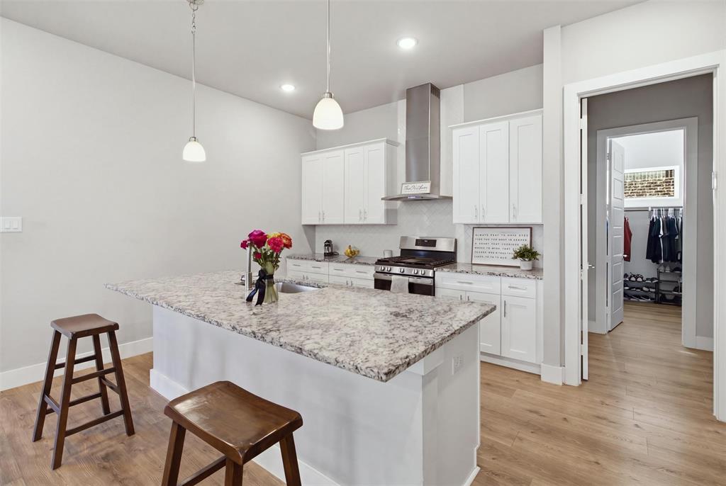 Kitchen featuring white cabinetry, stone countertops, stainless steel range with chimney-style hood, pendant lighting, and wood-finish flooring