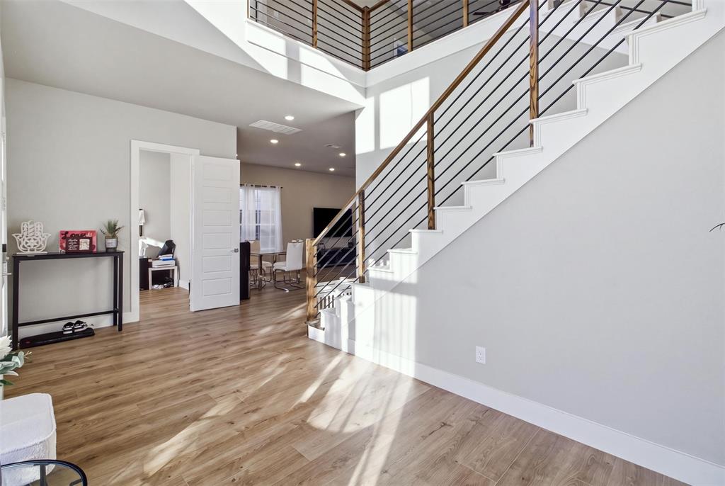 Two-story foyer featuring wood-finish flooring, a staircase with metal horizontal balusters, a wooden handrail, and recessed lighting