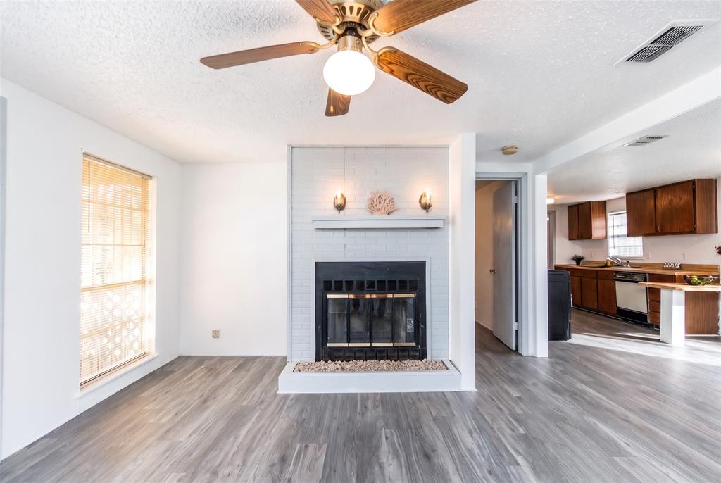 Fireplace with painted brick surround and integrated mantel, wood-finish flooring, and ceiling fan with light fixture Fireplace with painted brick surround and integrated mantel, wood-finish flooring, and ceiling fan with light fixture