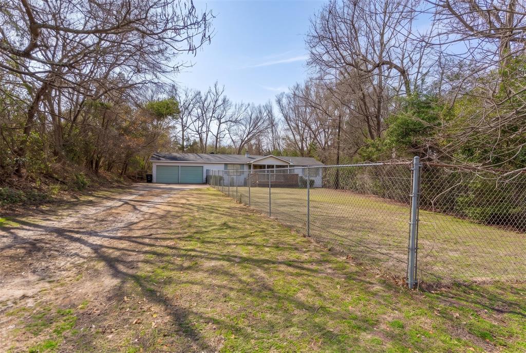 Single-story exterior featuring a two-car garage, fenced yard, and expansive grounds surrounded by mature trees