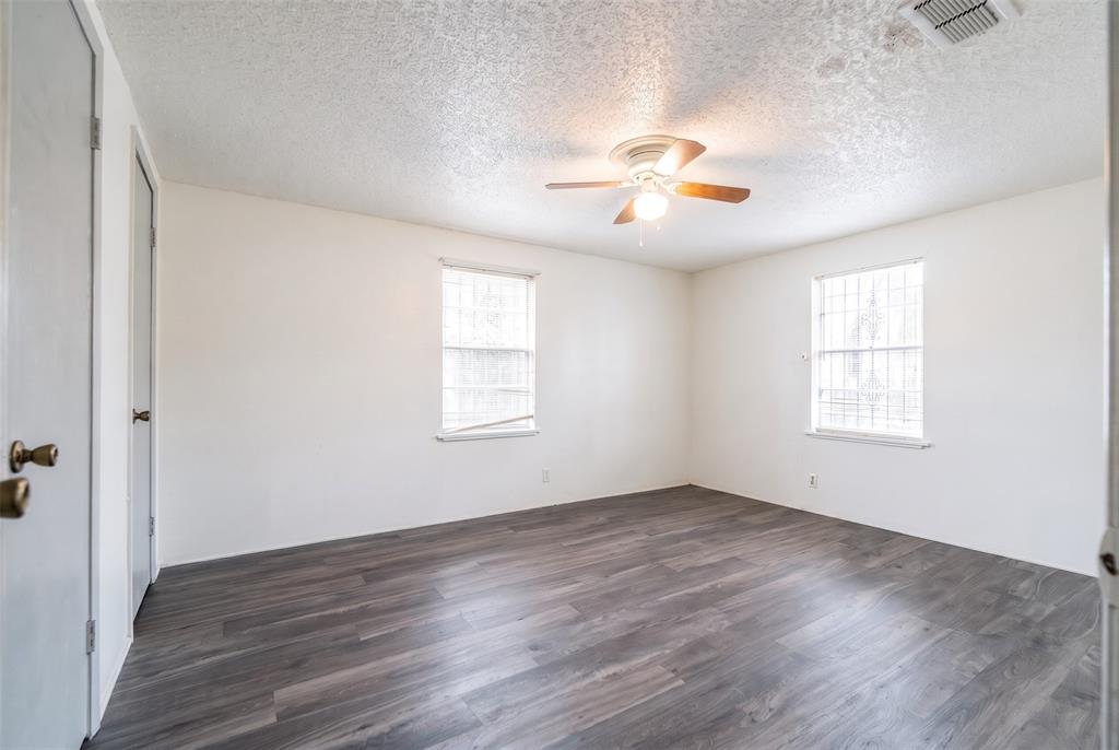 Interior room featuring wood-finish flooring, two dual-pane windows with metal security bars, and a ceiling-mounted light fixture with a fan