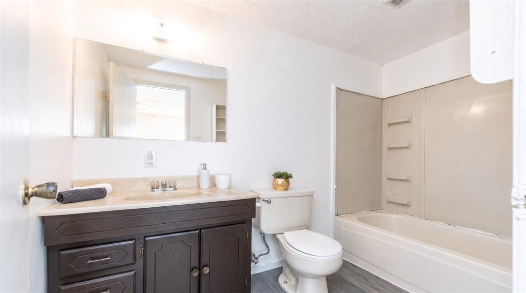 Bathroom featuring a dark wood-finish vanity, stone-surface countertop with an integrated basin, wall-mounted mirror, and a tub-shower combination with surround panels