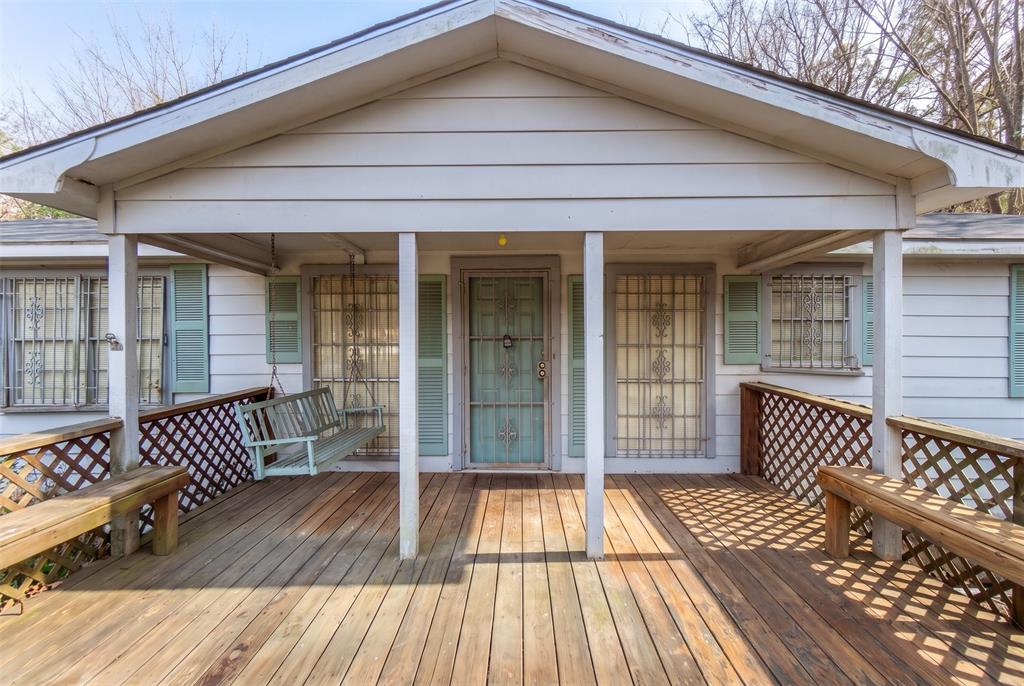 Covered front porch featuring wood-finish decking, lattice railings, built-in bench seating, and decorative metal security screens on windows and entry door