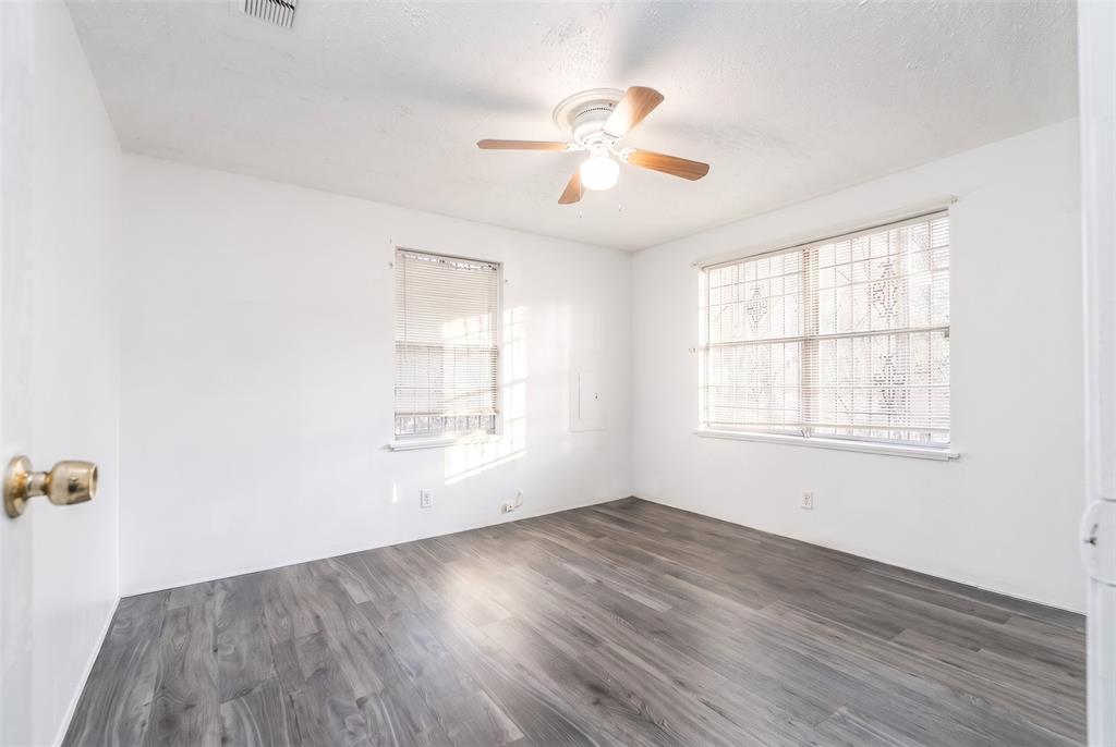 Neutral-toned room featuring wood-finish flooring, a ceiling fan with integrated light fixture, two windows, and security bars