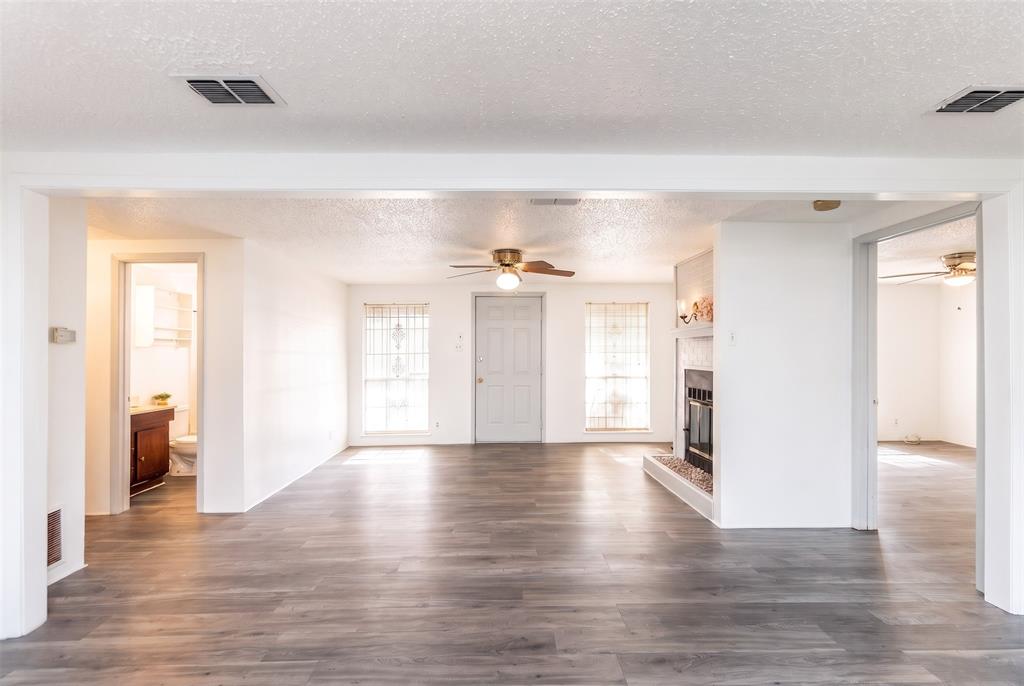 Open-concept area featuring wood-finish flooring, a painted brick fireplace with a raised hearth, and neutral wall tones Open-concept area featuring wood-finish flooring, a painted brick fireplace with a raised hearth, and neutral wall tones