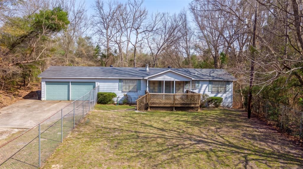 Single-story exterior featuring a wood deck, two-car garage, concrete driveway, and chain-link perimeter fencing