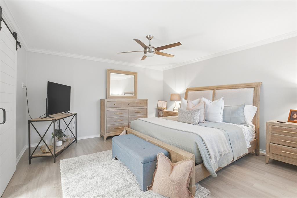 Room featuring light wood-finish flooring, white sliding barn door with black hardware, and a ceiling fan with integrated lighting Room featuring light wood-finish flooring, white sliding barn door with black hardware, and a ceiling fan with integrated lighting