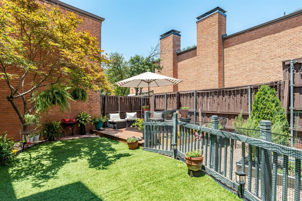 Fenced backyard featuring synthetic turf, wood-finish decking, mature trees, and brick exterior walls Fenced backyard featuring synthetic turf, wood-finish decking, mature trees, and brick exterior walls