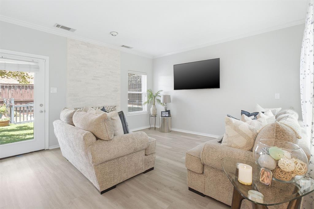 Living space featuring light wood-finish flooring, a floor-to-ceiling stone-textured fireplace surround, and a glass-paneled exterior door Living space featuring light wood-finish flooring, a floor-to-ceiling stone-textured fireplace surround, and a glass-paneled exterior door