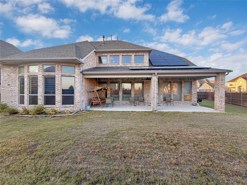 Brick exterior rear elevation featuring a covered patio, solar panels, and multi-pane window configurations