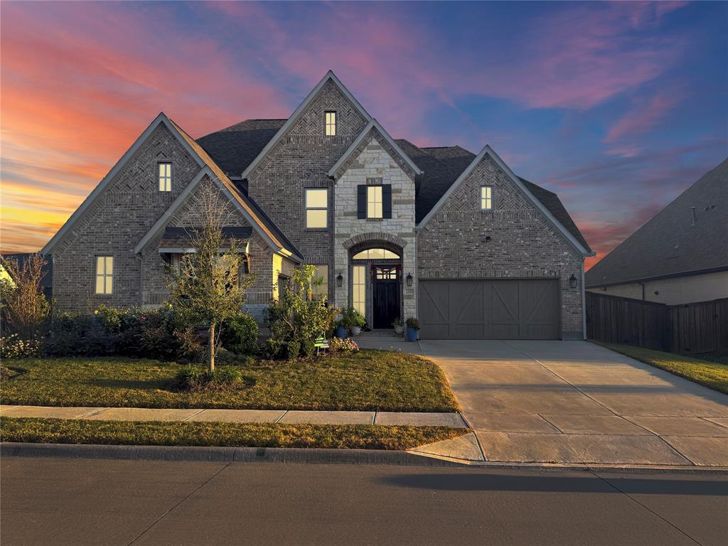 Multi-gabled exterior featuring brick and stone masonry, decorative shutters, arched entryway, and attached garage Multi-gabled exterior featuring brick and stone masonry, decorative shutters, arched entryway, and attached garage