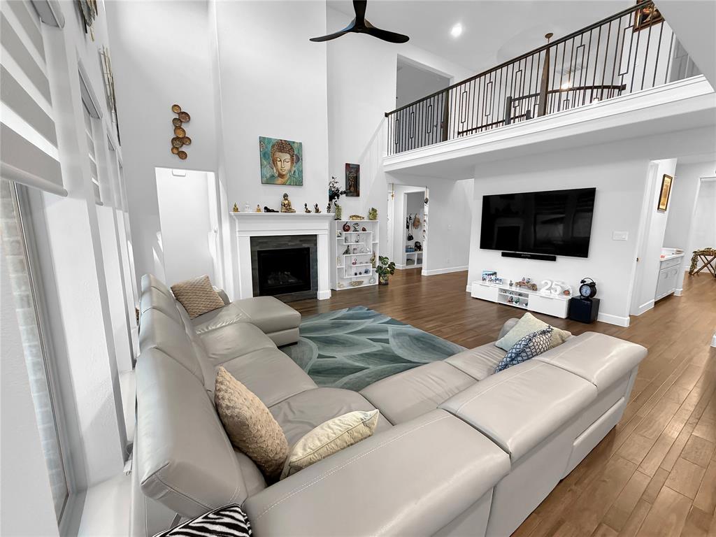 High-ceiling interior featuring a dark-tiled fireplace surround, wood-finish flooring, a matte black ceiling fan, and a mezzanine level with a metal railing