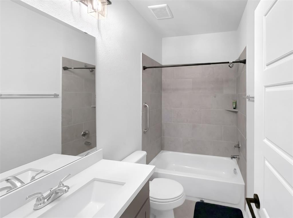 Bathroom featuring a vanity with a white rectangular sink and light-toned countertop, a frameless wall mirror, a bathtub with neutral tile surround, and a metal safety grab bar