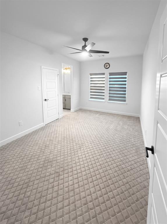 Interior room featuring textured carpet flooring, dual windows with adjustable roller shades, and a ceiling fan with integrated lighting