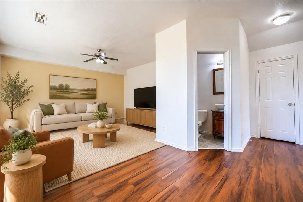 Wood-finish flooring, ceiling fan with integrated lighting, and a doorway leading to a bathroom featuring a wood-finish vanity and vessel sink