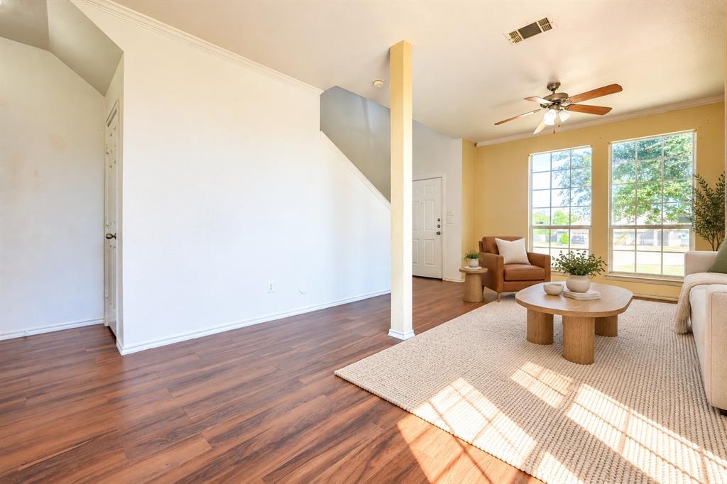 Living space featuring wood-finish flooring, a ceiling fan with integrated lighting, dual windows, and an exposed structural column