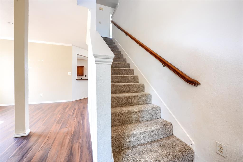 Carpeted staircase featuring a wood-finish handrail and white wall-mounted balustrade, complemented by wood-finish flooring and a structural column