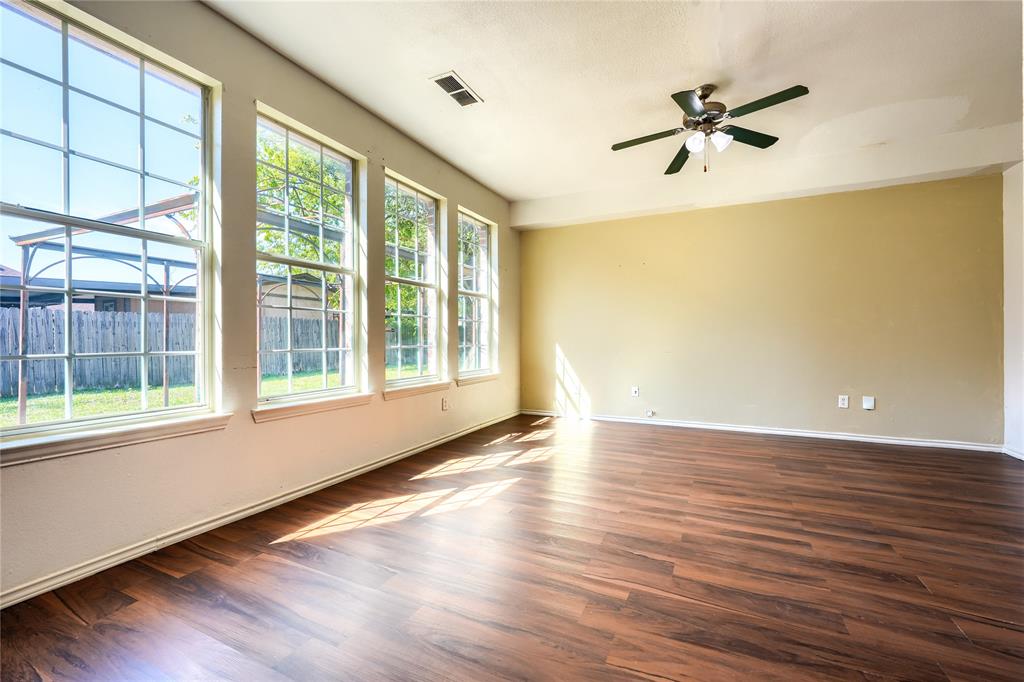Spacious room featuring wood-finish flooring, a ceiling fan with integrated lighting, and multiple large windows