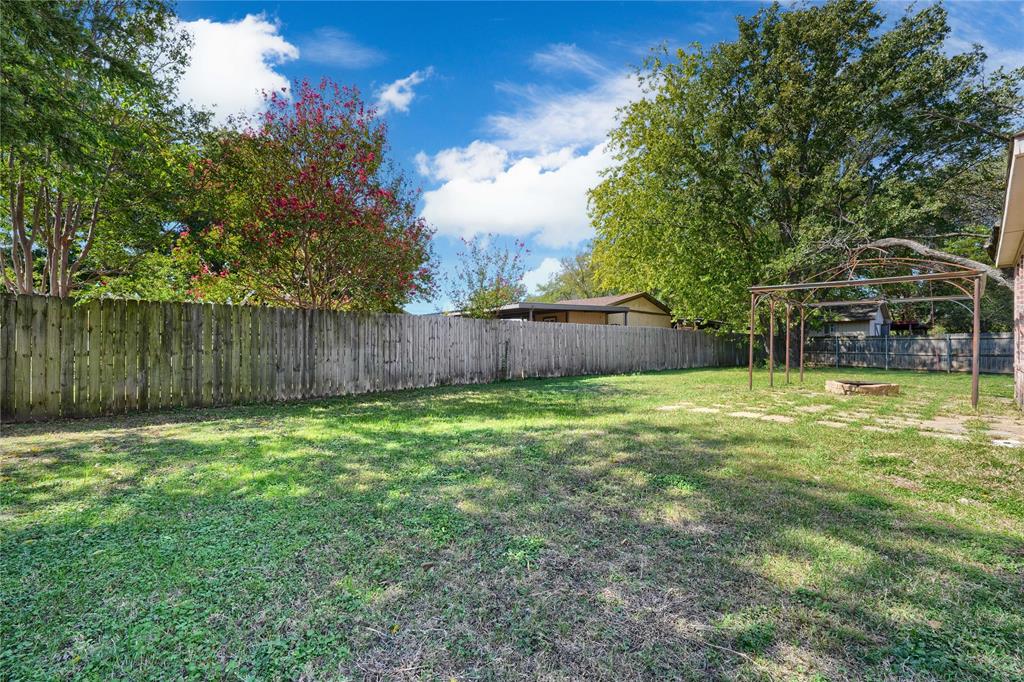 Backyard featuring an expansive lawn, wooden privacy fencing, a metal-frame arbor, and mature trees