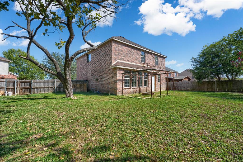 Brick exterior property featuring a large backyard, mature trees, wood privacy fencing, and a metal-frame pergola