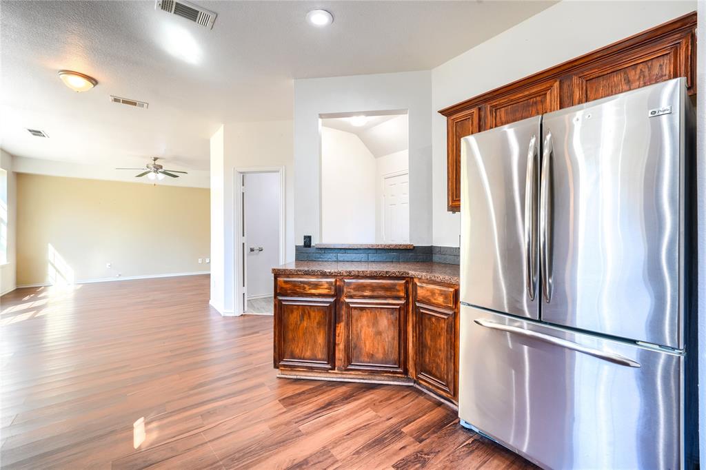 Kitchen featuring stained wood cabinetry, stone-surface countertops, and a built-in stainless steel refrigerator, complemented by wood-finish flooring