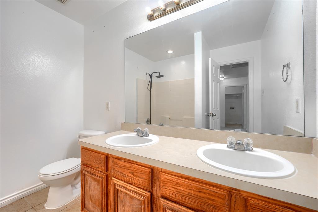 Bathroom featuring a double-sink vanity with wood cabinetry, a solid surface countertop, an expansive wall-mounted mirror, and a walk-in shower