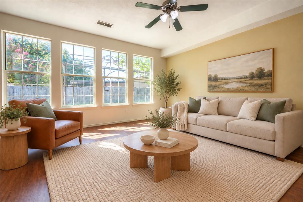 Living area featuring wood-finish flooring, a tray ceiling with a mounted light fixture and fan, and expansive grid-pane windows
