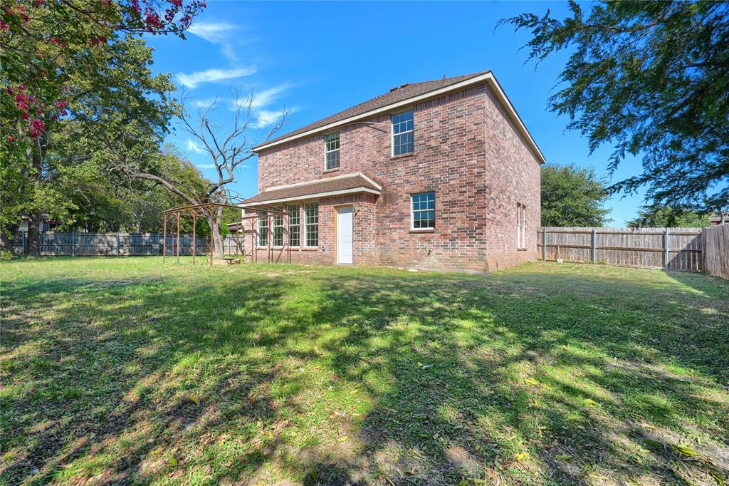 Two-story brick exterior featuring a shingled roof, multiple windows with grid detailing, and a fenced-in rear yard