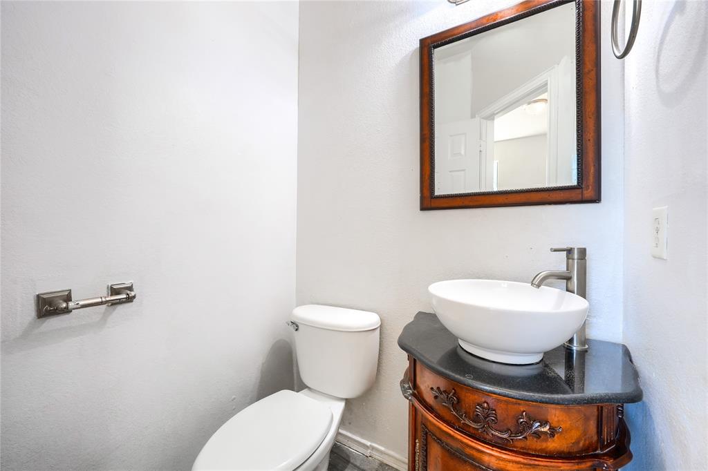 Powder room featuring a wood-finish vanity with ornate detailing, a dark stone countertop, a white oval vessel sink, a brushed-nickel faucet, and a wall-mounted framed mirror