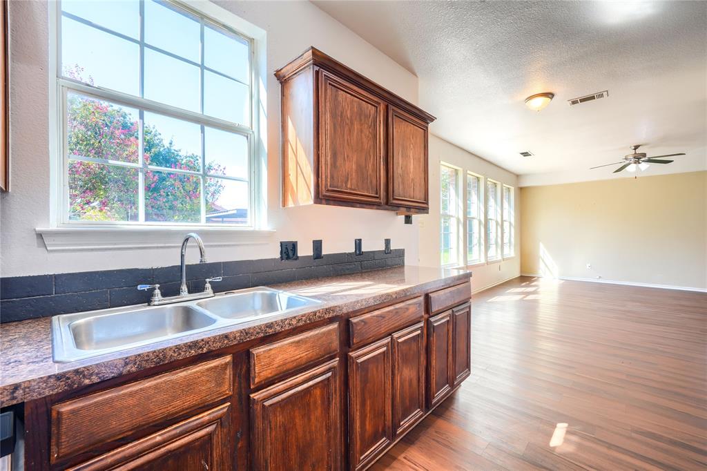 Kitchen featuring dark wood-finish cabinetry, a dual-basin stainless steel sink with a high-arch faucet, a stone-composite countertop, and a dark tile backsplash