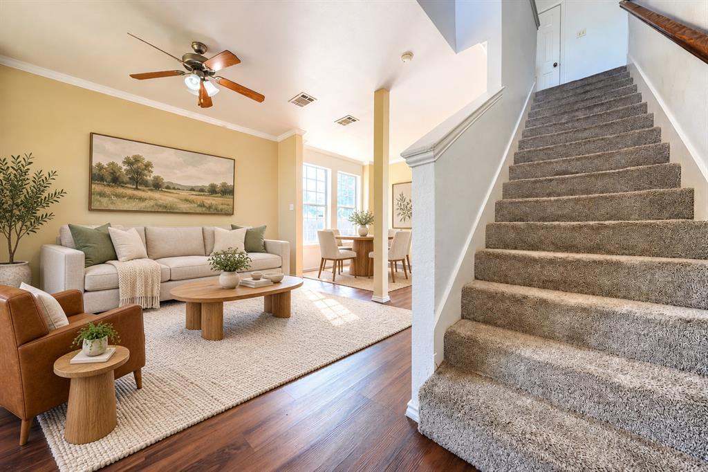 Interior featuring wood-finish flooring, carpeted stairs with a wooden handrail, and a ceiling fan with integrated lighting