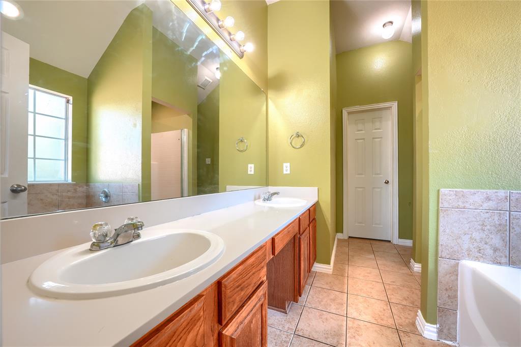 Double vanity featuring light-toned solid surface countertops, wood cabinetry, tile flooring, and a full-width wall mirror