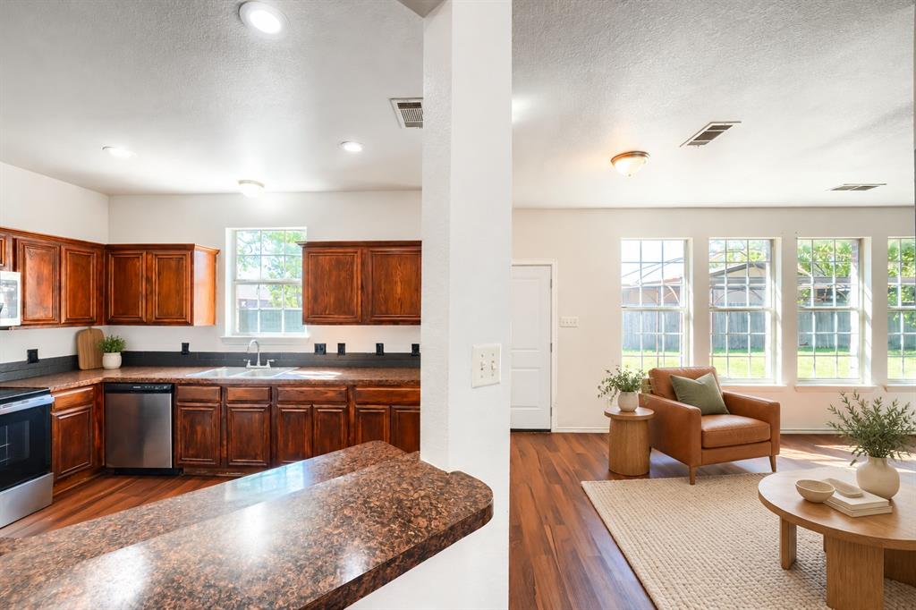Kitchen featuring stained wood cabinetry, stone-finish countertops, stainless steel appliances, wood-finish flooring, and multiple windows