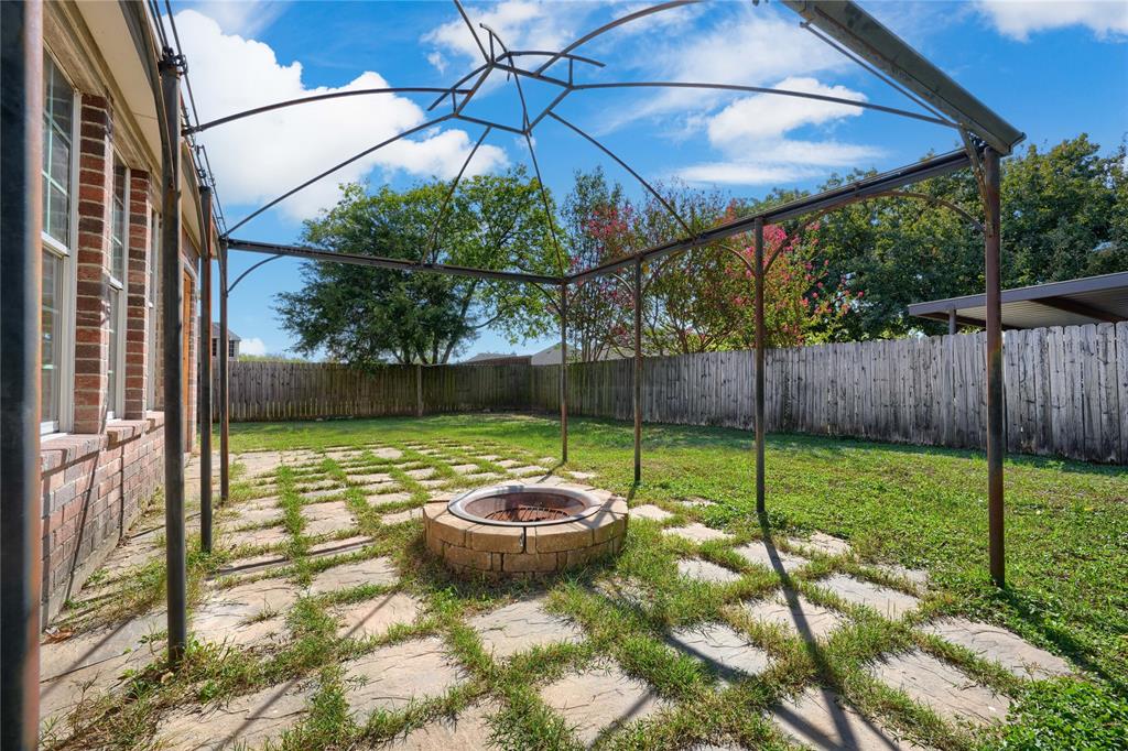 Backyard featuring a metal frame pergola, a circular stone fire pit, grid-patterned stone pavers, and a perimeter wood fence