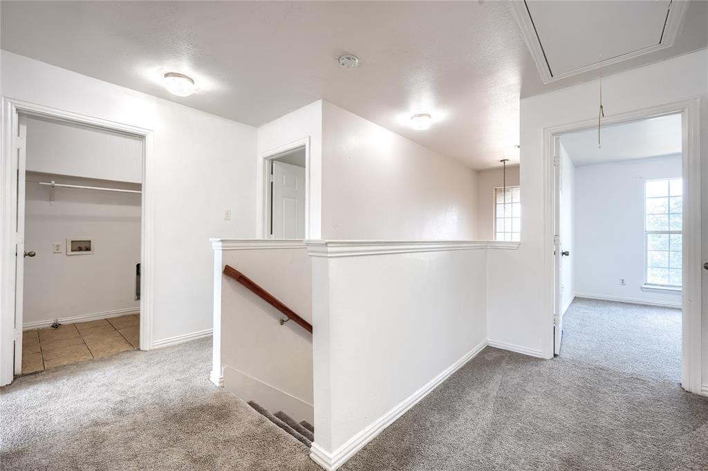 Hallway featuring neutral carpeting, a staircase with a wooden handrail, flush-mount ceiling lighting, and multiple interior doorways