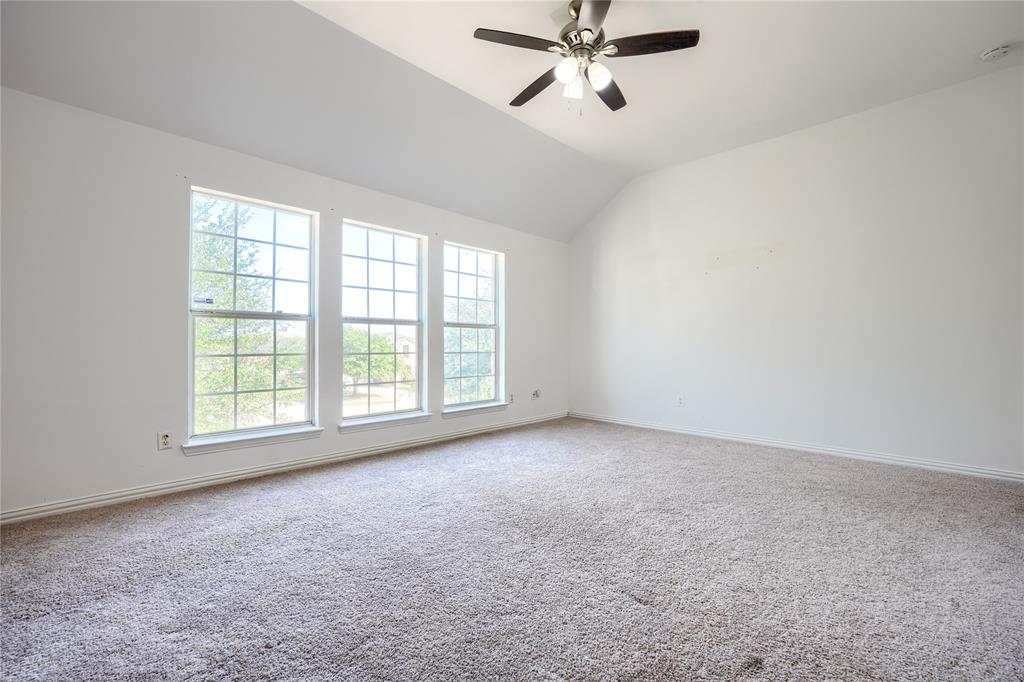 Vaulted ceilings featuring a multi-light ceiling fan and three large grid-pattern windows with neutral carpeting