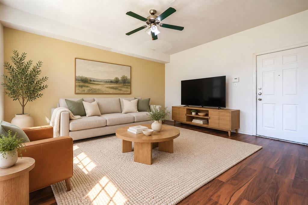Living area featuring wood-finish flooring, a neutral-toned accent wall, and a multi-blade ceiling fan with integrated lighting