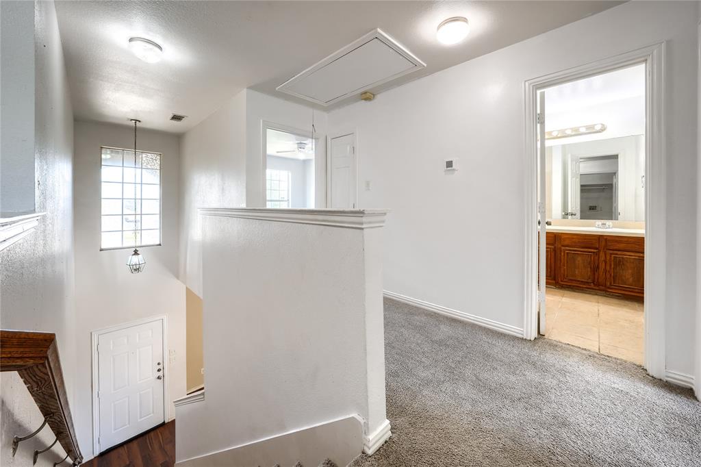 Multi-level interior featuring a carpeted landing, a tall window with grid detailing, a pendant light fixture, and a doorway revealing a bathroom with wood-finish cabinetry