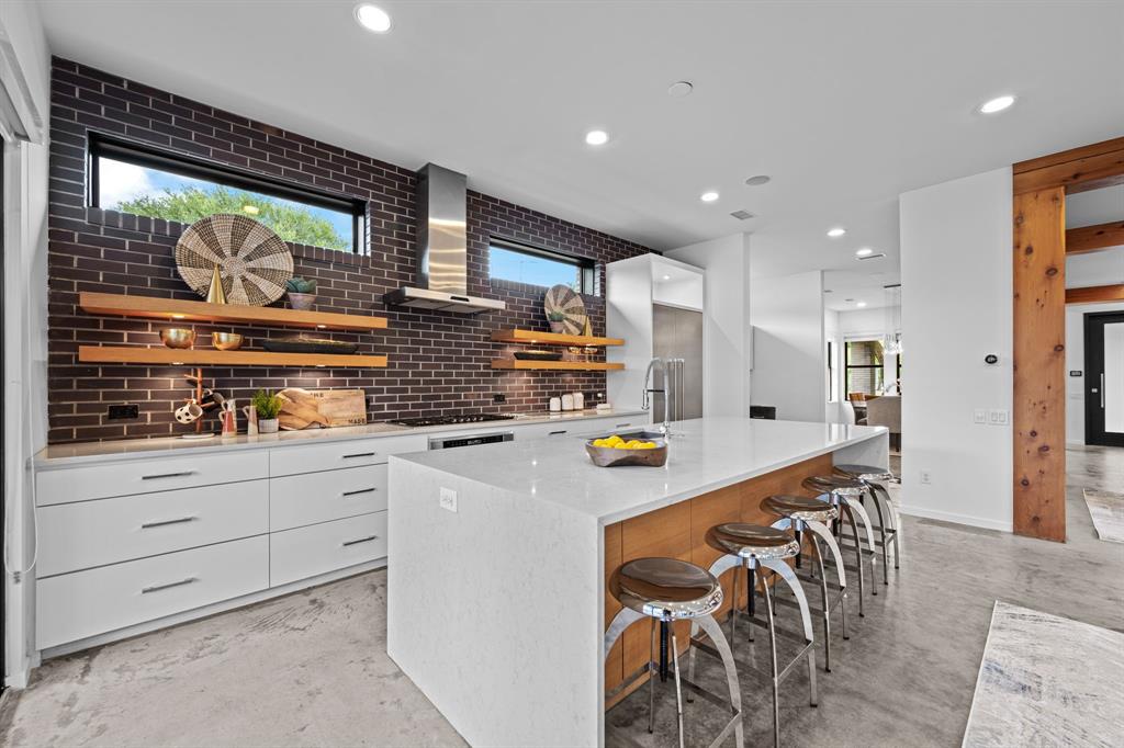 Rich brick, floating wood shelves, and waterfall countertops give the kitchen its distinctive personality.