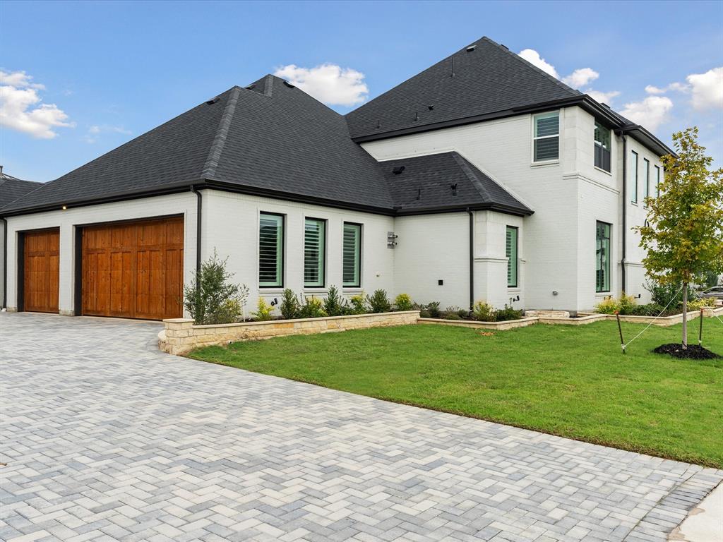 Two-story residence featuring white painted brick exterior, multi-hipped asphalt shingle roof, stone-accented hardscaping, and double wood-finish garage doors