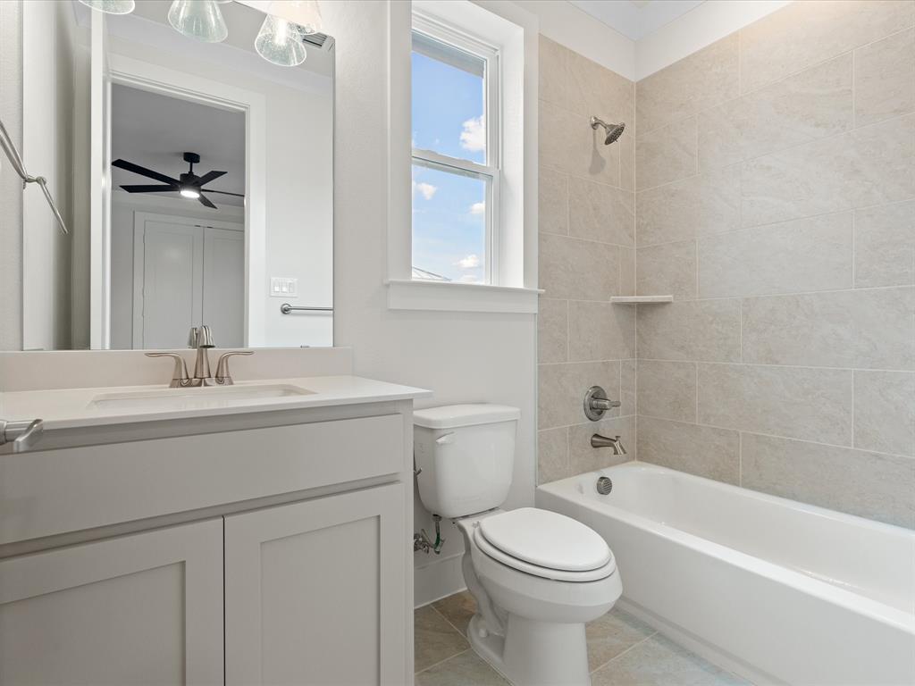 Bathroom featuring a vanity with a white countertop and undermount sink, tiled bathtub surround with a built-in shelf, brushed nickel hardware, and neutral tile flooring