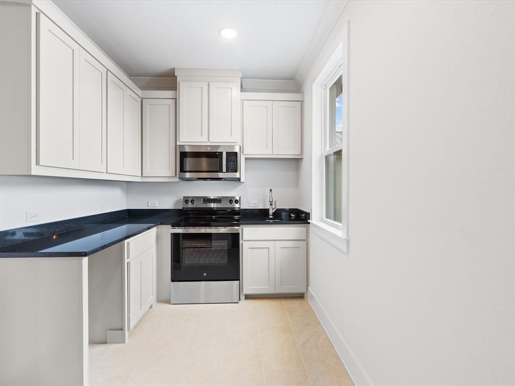 Kitchen featuring white shaker-style cabinetry, dark stone countertops, stainless steel appliances, and tile flooring