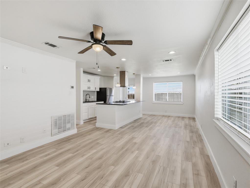 Open-concept interior featuring wood-finish flooring, recessed lighting, a ceiling fan with integrated light fixture, kitchen island with stone-finish countertop, and white cabinetry with a tile backsplash Open-concept interior featuring wood-finish flooring, recessed lighting, a ceiling fan with integrated light fixture, kitchen island with stone-finish countertop, and white cabinetry with a tile backsplash