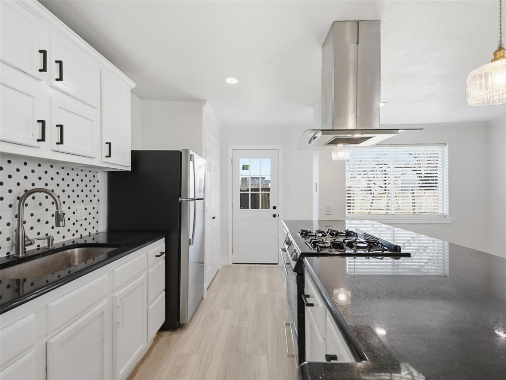 Kitchen featuring white cabinetry with matte black hardware, dark stone countertops, a geometric patterned backsplash, stainless steel gas cooktop with a chimney-style range hood, and wood-finish flooring