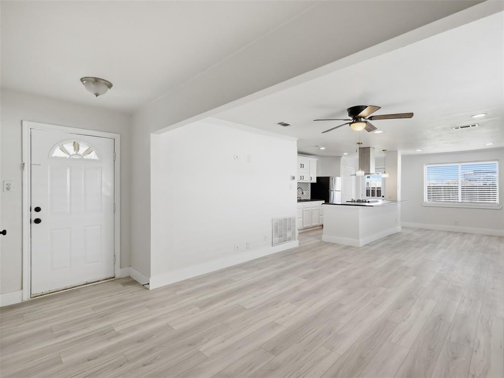 Open-concept interior featuring light wood-finish flooring, recessed lighting, ceiling fans, and a kitchen island with a stainless steel range hood Open-concept interior featuring light wood-finish flooring, recessed lighting, ceiling fans, and a kitchen island with a stainless steel range hood